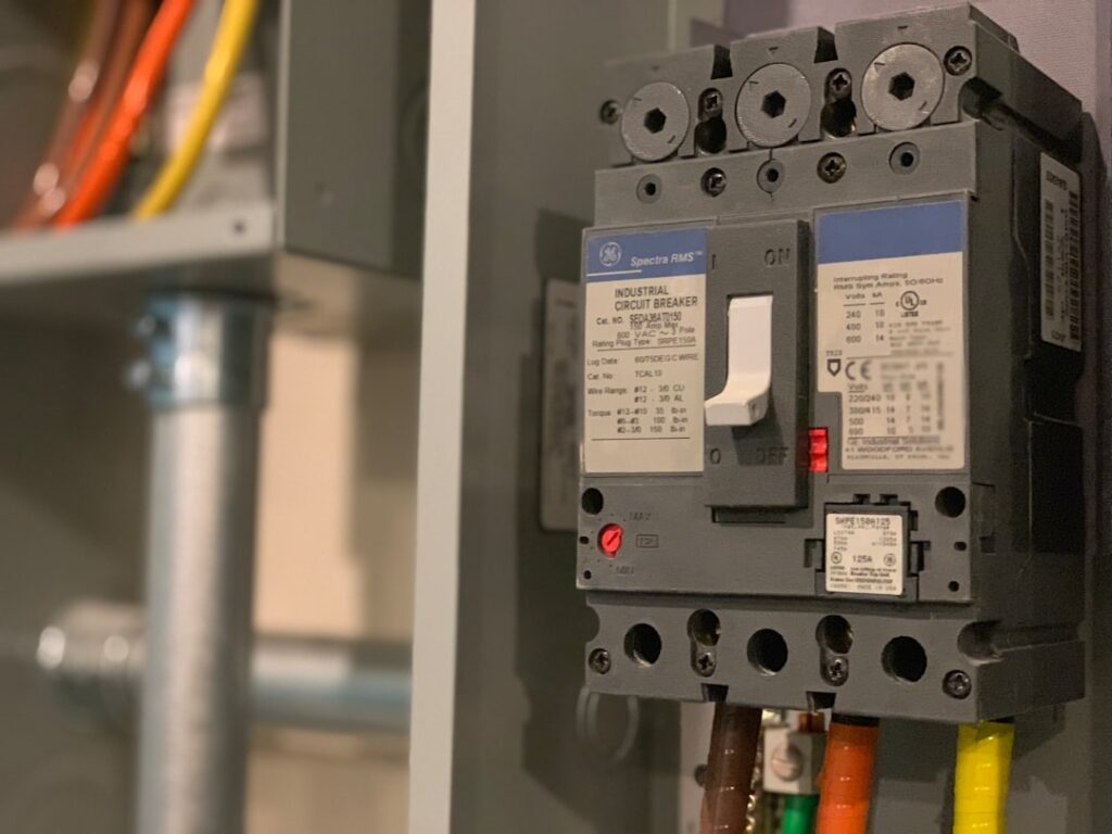 A close-up of a homeowner switching a generator transfer switch beside a main electrical panel indoors.